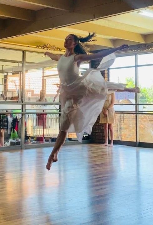 A dancer mid-jump in the sunlit studio