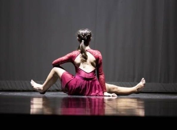 A dancer seated on stage in a deep red dress