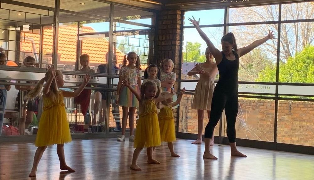 Small children in yellow dresses copying their teacher